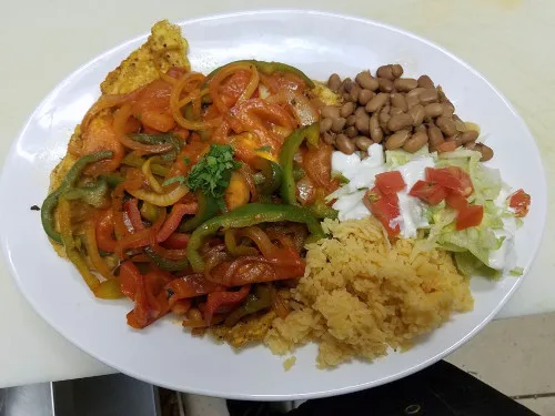 A plate of peppers, onions, beans, rice and sour cream