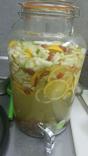 A large jar of agua fresca with lemon, cucumber and fruit