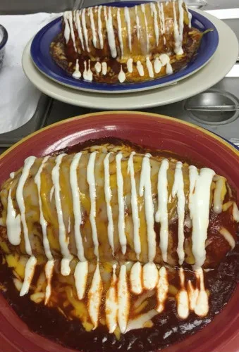 A burrito in red sauce striped with crema on a red plate