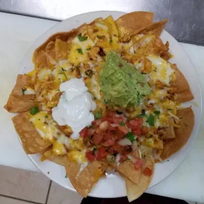 Nachos with melted cheese, guacamole, sour cream and pico de gallo on a white plate