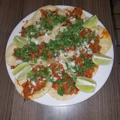 A plate of tacos topped with cilantro and onion, ringed with lime wedges