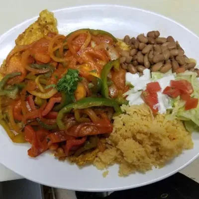 A plate of peppers and onions in sauce beside beans, rice and sour cream