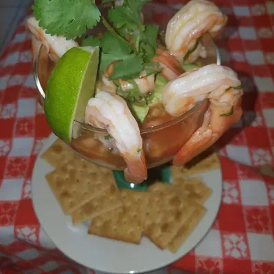 A shrimp cocktail with cilantro and a lime wedge, beside a stack of crackers