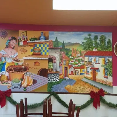 A painted wall mural of a Mexican village street, with a red-bowed garland below