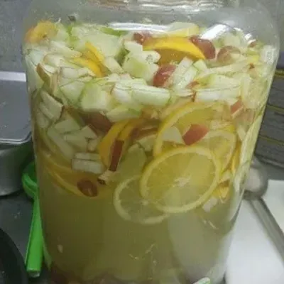 A large glass jar of agua fresca with lemon slices, cucumber and fruit