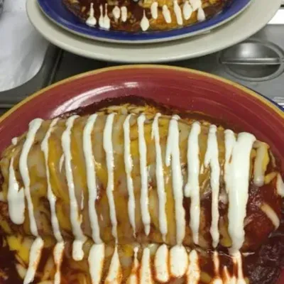 A burrito in red sauce striped with crema, on a red plate