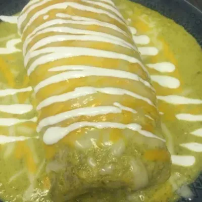 A burrito smothered in green sauce and drizzled with crema