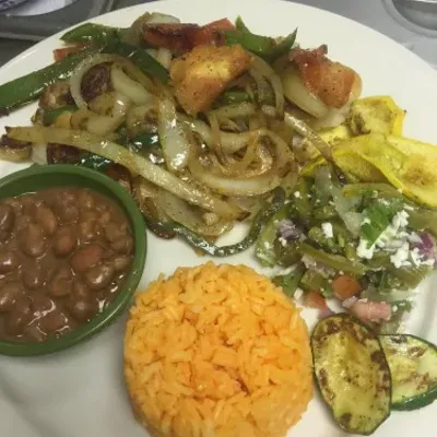 Sautéed peppers, onions and grilled zucchini beside a bowl of beans and orange rice