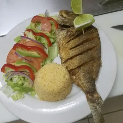 A whole grilled fish with lime, salad and rice on a white plate